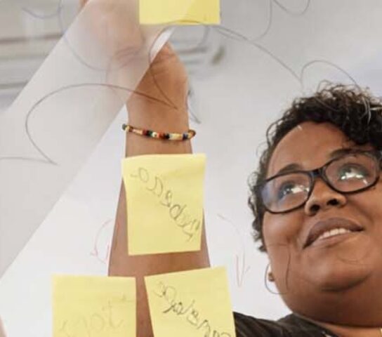 Two people placing Post It notes on a clear board