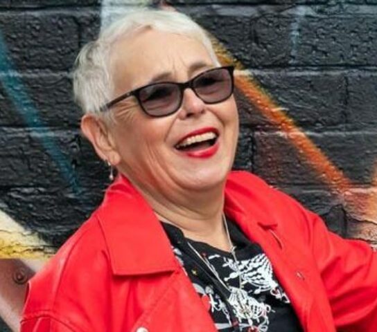 Older person wearing red jacket and glasses bya graffiti wall