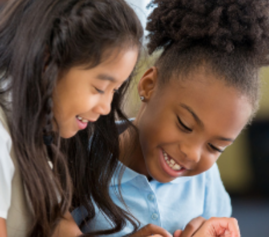 Two children looking at a book in a classroom.