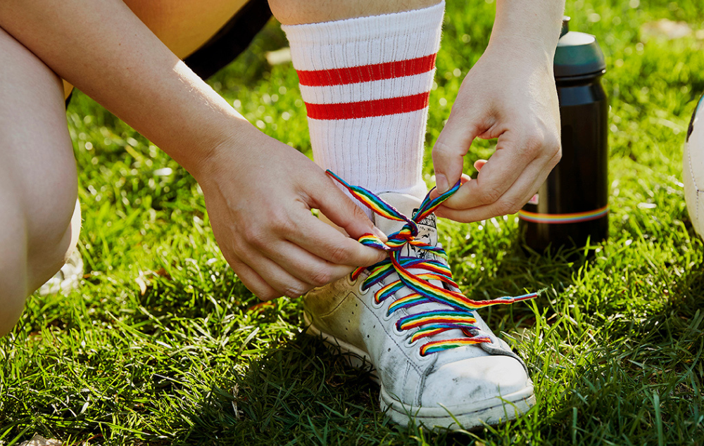 Two hands tying a trainer shoe which features rainbow laces.