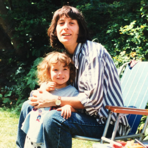 A white mother and child outside. The mother is sitting in a chair, the child is against her knees.