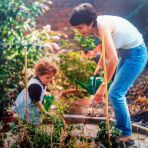 A white mother and child in a garden, tending flowers in sunshine. The picture is taken on old-style film.