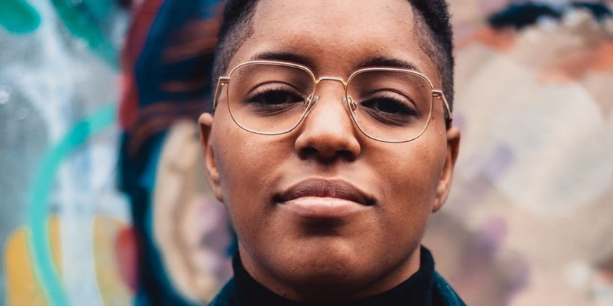 A person in glasses in front of a colourful mural.