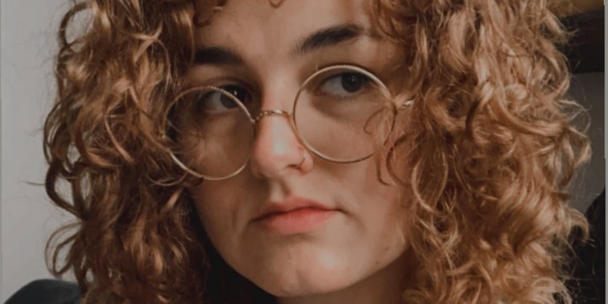 A person in round-frame glasses with long wavy brown hair.