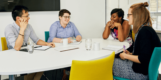 Four people sitting around a table in a workplace meeting room