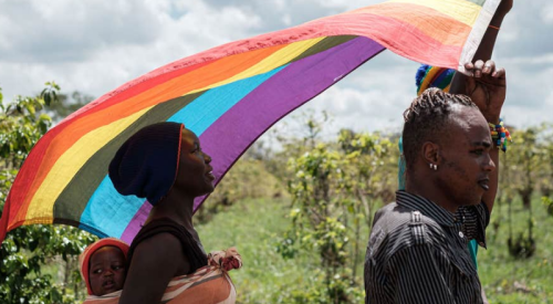 Two Black people with a rainbow flag in a field