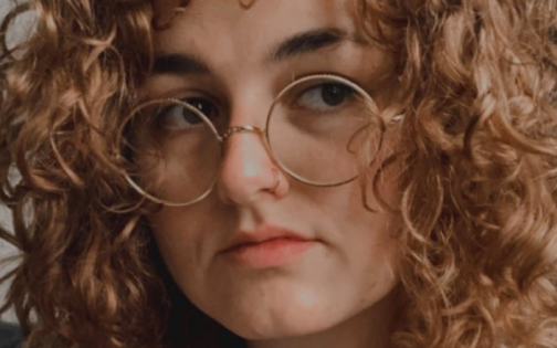 Person with long curly hair and glasses