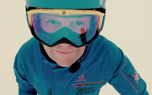 Person in skiing uniform wearing goggles on snow and looking up at the camera