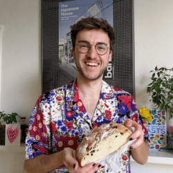 Person wearing a loud shirt and holding a loaf of bread, and smiling